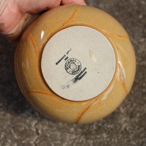 May include: A yellow ceramic bowl with a white base. The bowl has a raised design around the rim and a black stamp on the bottom that reads "BOGANAS APTIT 400 BOGANAS POTTERY SWEDEN".