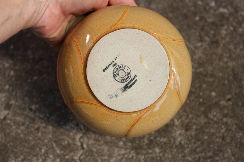 May include: A yellow ceramic bowl with a white base. The bowl has a raised design around the rim and a black stamp on the bottom that reads "BOGANAS APTIT 400 BOGANAS POTTERY SWEDEN".