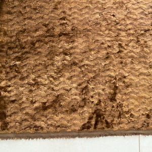 May include: A close-up of a brown, textured fabric with a subtle sheen. The fabric has a wavy pattern and a soft, plush feel.