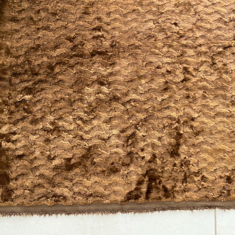 May include: A close-up of a brown, textured fabric with a subtle sheen. The fabric has a wavy pattern and a soft, plush feel.