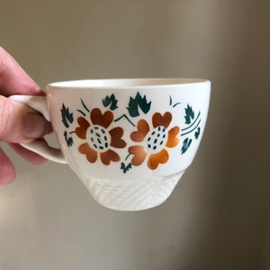 Peut inclure: Une tasse &agrave; th&eacute; en c&eacute;ramique blanche avec un motif floral compos&eacute; de deux fleurs orange avec des feuilles vertes.