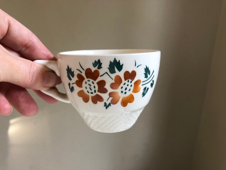 Peut inclure: Une tasse &agrave; th&eacute; en c&eacute;ramique blanche avec un motif floral compos&eacute; de deux fleurs orange avec des feuilles vertes.
