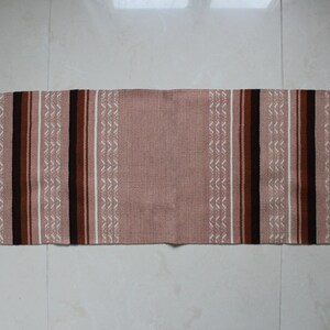 May include: A long, narrow rug with a pink background and brown, black, and white stripes. The rug has a fringe on both ends.