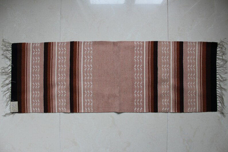 May include: A long, narrow rug with a pink background and brown, black, and white stripes. The rug has a fringe on both ends.