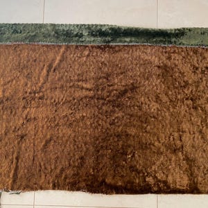 May include: A brown fuzzy fabric with a green velvet border. The fabric has a soft, plush texture.