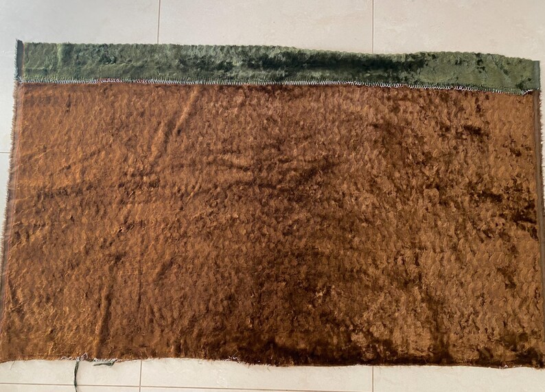 May include: A brown fuzzy fabric with a green velvet border. The fabric has a soft, plush texture.