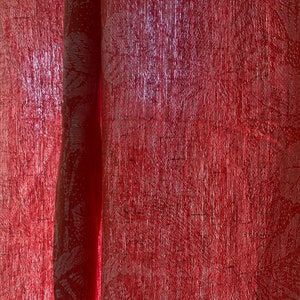 May include: Close-up of a red sheer curtain with a subtle pattern. The curtain is slightly translucent, allowing some light to shine through.