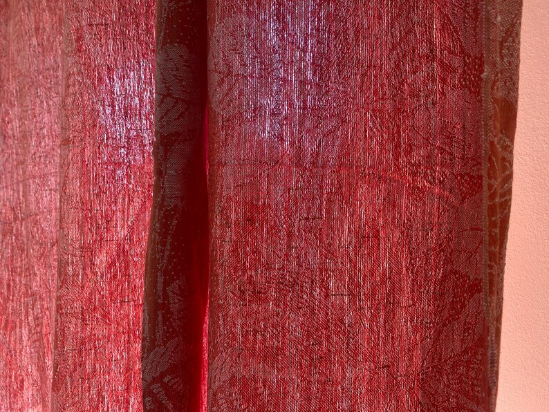 May include: Close-up of a red sheer curtain with a subtle pattern. The curtain is slightly translucent, allowing some light to shine through.