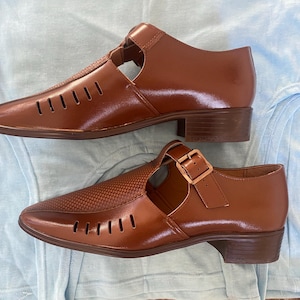 May include: Two pairs of brown leather sandals with cutouts and buckles. The sandals have a low heel and a closed toe.