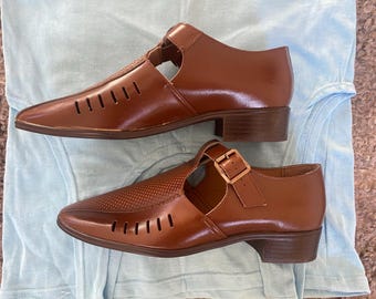 May include: Two pairs of brown leather sandals with cutouts and buckles. The sandals have a low heel and a closed toe.