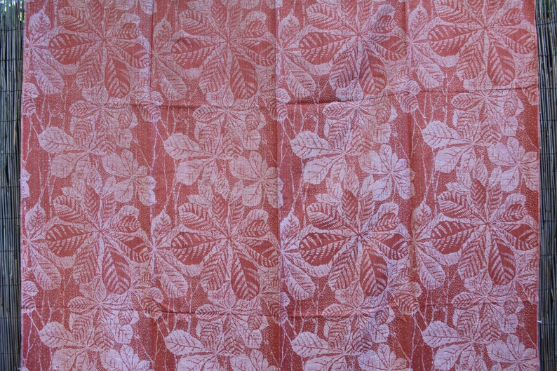 May include: A red fabric with a white leaf pattern. The leaves are arranged in a repeating pattern and have a slightly textured look.