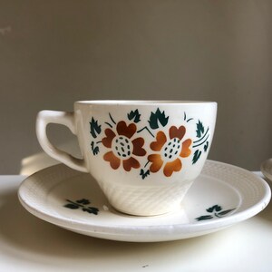 Peut inclure: Une tasse &agrave; th&eacute; et une soucoupe blanches avec un motif floral. La tasse a un motif floral vert et marron avec deux grandes fleurs. La soucoupe a un motif floral assorti.