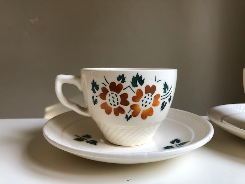Peut inclure: Une tasse &agrave; th&eacute; et une soucoupe blanches avec un motif floral. La tasse a un motif floral vert et marron avec deux grandes fleurs. La soucoupe a un motif floral assorti.
