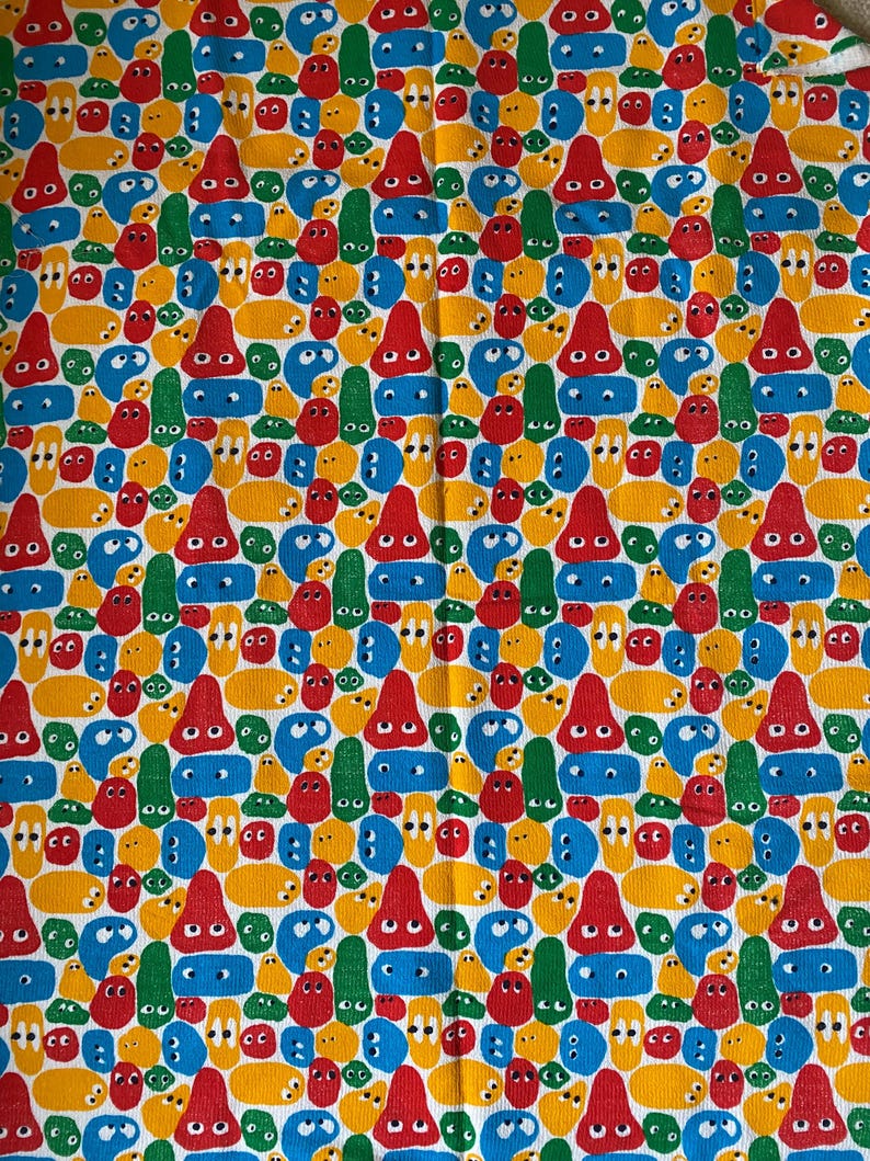 Pu&ograve; includere: Un tessuto colorato con un motivo ripetuto di facce e forme di cartoni animati in rosso, giallo, blu e verde. Il design presenta nasi rossi a forma di cono e varie forme di occhi, creando un'estetica giocosa e stravagante.