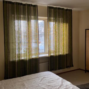 May include: Two floor-length window curtains featuring vertical stripes in shades of olive green, brown, and thin accents of yellow and blue. The fabric is semi-sheer with a textured weave, hanging from a white rod over a window frame.