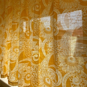 May include: Yellow sheer curtains with a white sunflower pattern. The curtains are made of a lightweight fabric and have a delicate, flowing drape.