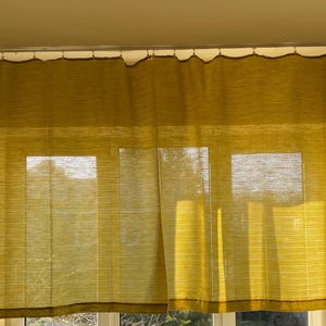 May include: Yellow sheer curtains hanging in a window. The curtains are made of a thin, woven fabric and have a subtle texture. The curtains are letting in natural light, creating a soft, diffused glow in the room.