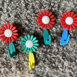 May include: Five flower-shaped hooks in red, green, and blue with white centers. The hooks are designed to look like flowers and have a stem and a hook at the bottom.