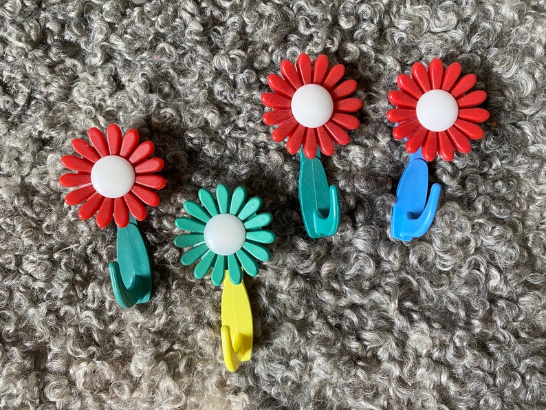 May include: Five flower-shaped hooks in red, green, and blue with white centers. The hooks are designed to look like flowers and have a stem and a hook at the bottom.