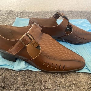 May include: Two pairs of brown leather sandals with cutouts and buckles. The sandals have a closed toe and a low heel.
