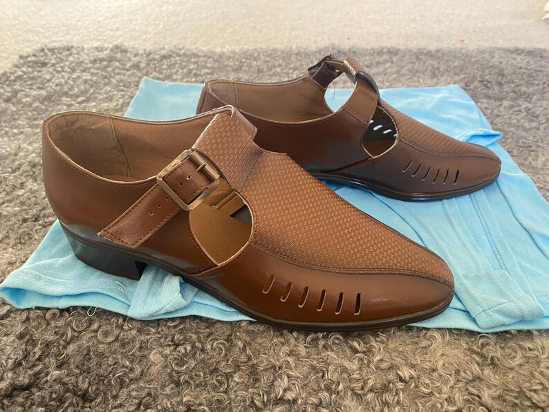 May include: Two pairs of brown leather sandals with cutouts and buckles. The sandals have a closed toe and a low heel.