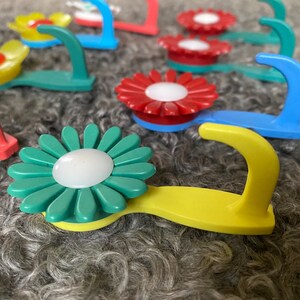 May include: Assortment of colorful flower-shaped hooks with a white center. The hooks are made of plastic and have a variety of colors, including red, blue, yellow, and green.