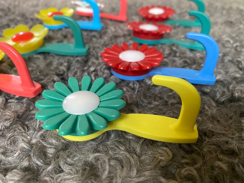 May include: Assortment of colorful flower-shaped hooks with a white center. The hooks are made of plastic and have a variety of colors, including red, blue, yellow, and green.