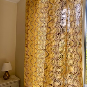 May include: A sheer curtain panel featuring a vibrant yellow base colour with vertical, wavy, dark brown lines running from top to bottom. The fabric has a textured, grid-like weave that allows light to pass through, creating a semi-transparent effect.
