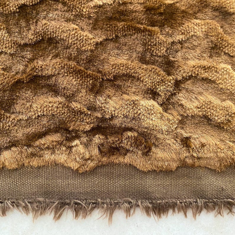 May include: A brown faux fur fabric with a wavy pattern. The fabric has a brown canvas backing and a fringe trim.