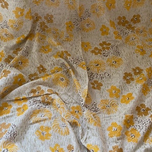May include: A beige fabric with a yellow floral pattern. The fabric has a textured, linen-like appearance.