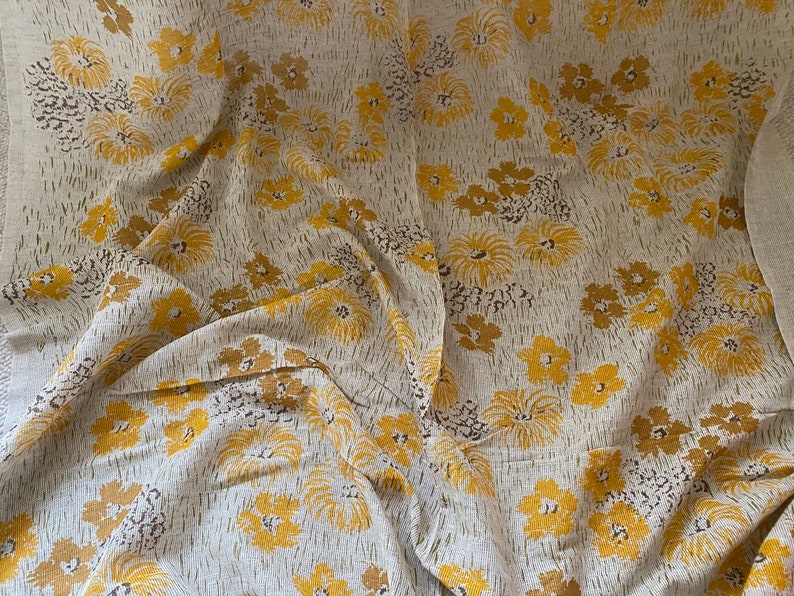 May include: A beige fabric with a yellow floral pattern. The fabric has a textured, linen-like appearance.
