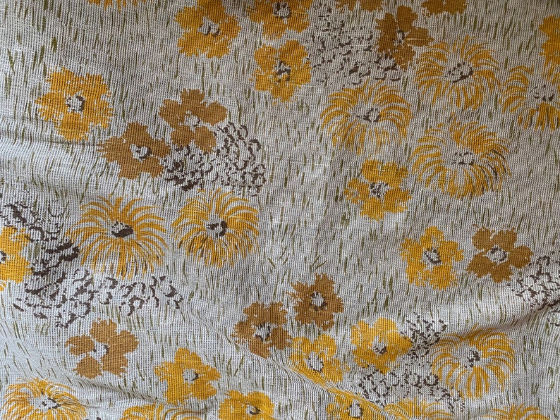 May include: A white fabric with a repeating pattern of yellow stylized flowers. The fabric has a textured, woven appearance.