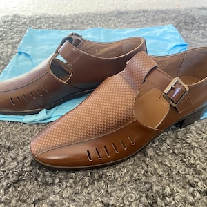 May include: A pair of brown leather sandals with cutouts and a buckle closure. The sandals have a textured pattern and a low heel.