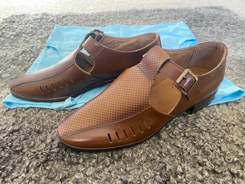 May include: A pair of brown leather sandals with cutouts and a buckle closure. The sandals have a textured pattern and a low heel.