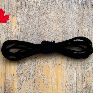 May include: A close-up of a black elastic cord, coiled and tied in the middle, against a light brown wooden background.