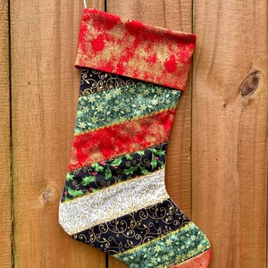 May include: A red, green, gold, and white Christmas stocking with a gold glitter pattern. The stocking is made of fabric and has a loop at the top for hanging.