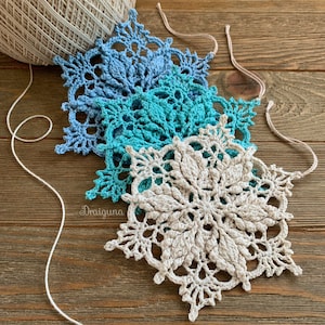 May include: Three crocheted snowflakes in shades of blue and white. The snowflakes are layered on top of each other, with the largest snowflake in the center.