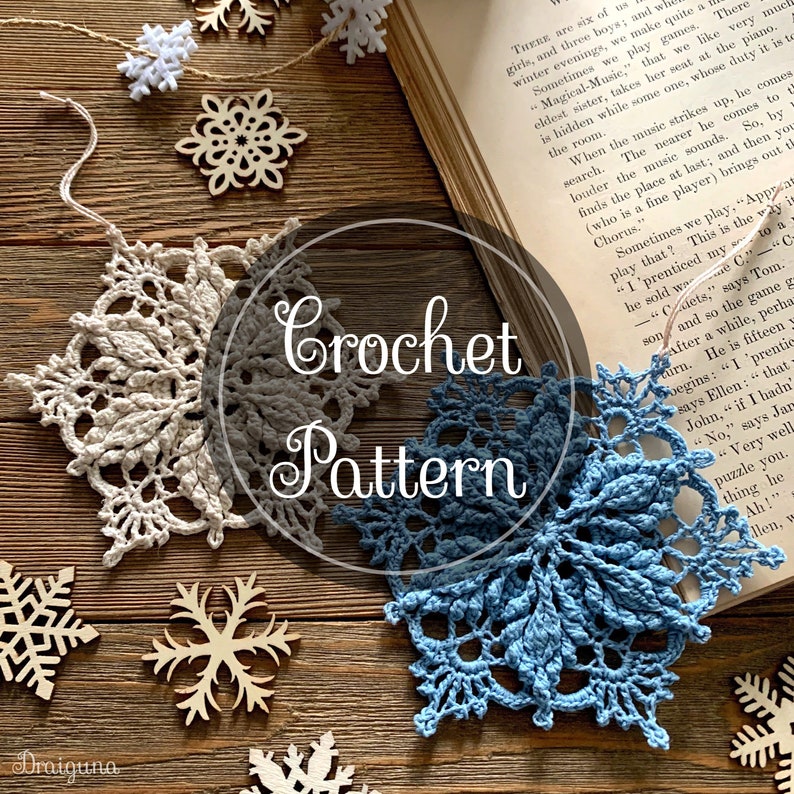 May include: Two crocheted snowflakes, one in beige and one in blue, are displayed on a wooden surface with several wooden snowflake ornaments. The text "Crochet Pattern" is written in a white circle on the image.