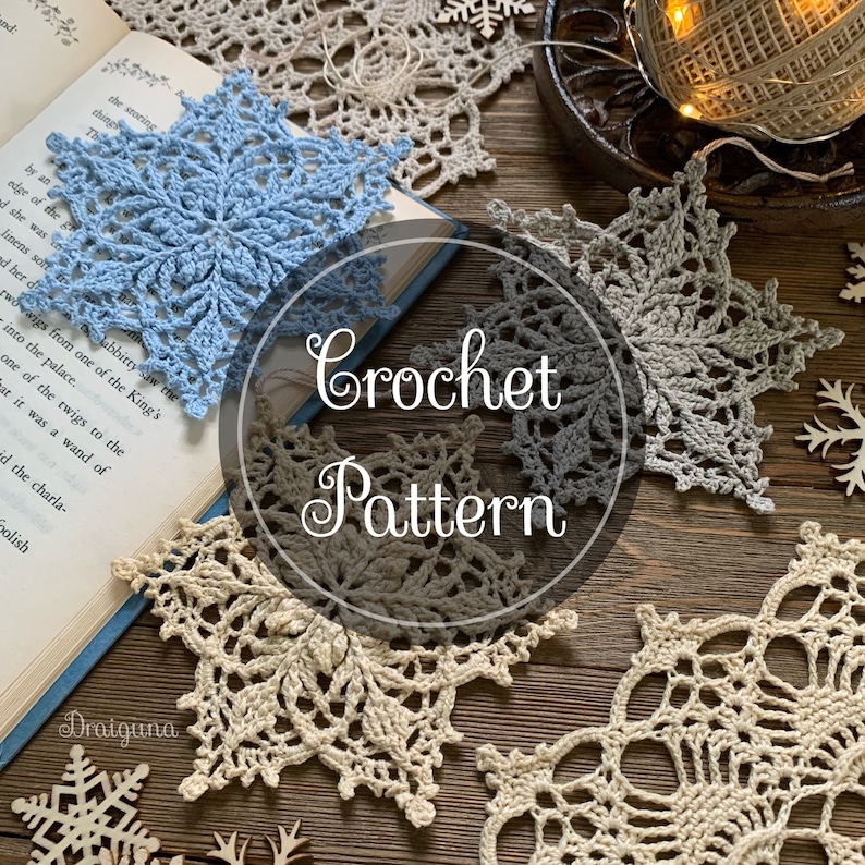 May include: Crochet pattern for a snowflake. The pattern is written on a book with a blue snowflake on top of it. There are four crocheted snowflakes in the image, two are white, one is gray, and one is blue.