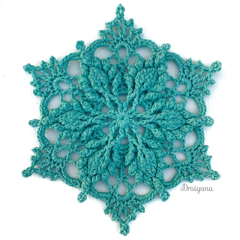 May include: A teal crocheted snowflake with a delicate, intricate design. The snowflake is made with a fine yarn and has a lacy appearance.
