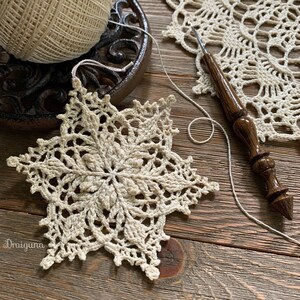 May include: A delicate crocheted snowflake ornament in a cream color, with a wooden crochet hook and a ball of yarn in the background.