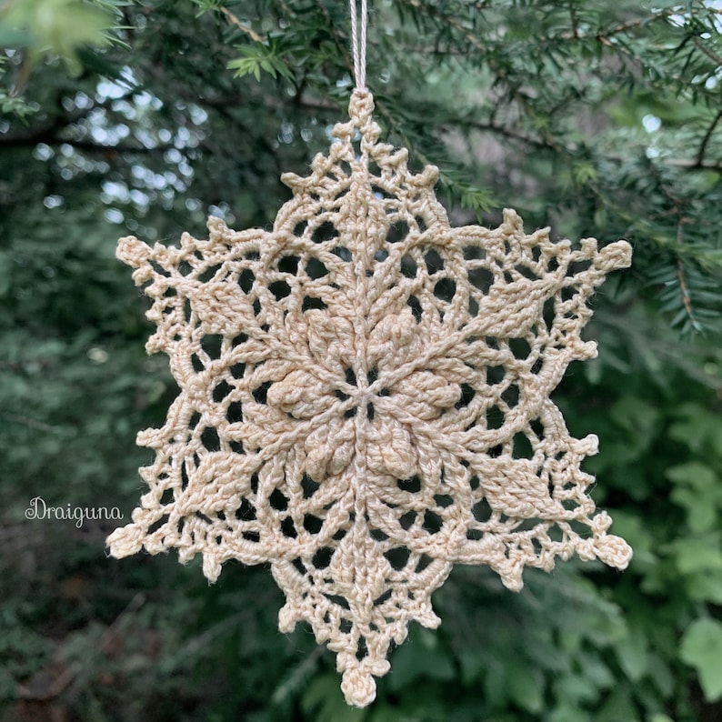 May include: A crocheted snowflake ornament in a cream color, hanging from a tree branch.
