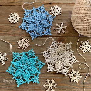 May include: Three crocheted snowflakes in blue, teal, and cream colors, with a ball of yarn and wooden snowflake ornaments on a wood background.