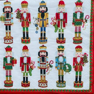 Puede incluir: Una servilleta blanca con un patrón repetido de figuras de cascanueces coloridos con varios atuendos. Los cascanueces sostienen regalos, bastones de caramelo y pequeños árboles de Navidad. La servilleta tiene un borde rojo y verde.