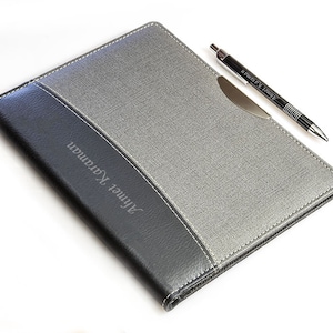 May include: A gray and black leatherette folder with a pen holder and the name "Ahmed Karam" embossed on the front.