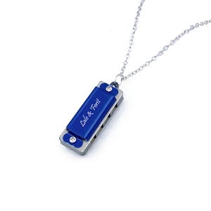 May include: A blue harmonica necklace with the inscription "Lale & Ferit" hanging from a silver chain.