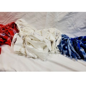 Pu&ograve; includere: Una collezione di ritagli di tessuto rosso, bianco e blu disposti su una superficie bianca. Il tessuto rosso &egrave; fantasia, il tessuto bianco &egrave; strutturato e il tessuto blu ha un effetto tie-dye. La disposizione ricorda una bandiera.