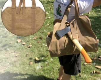 May include: A brown canvas log carrier with sturdy handles and reinforced stitching. An axe with a wooden handle and orange accents is placed in the carrier. The carrier is being held over a grassy area.