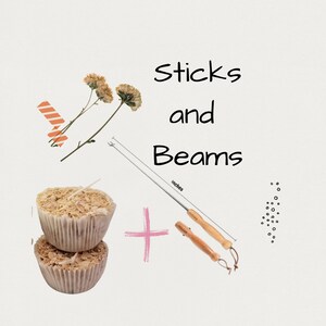 May include: The image features two cupcake-shaped candles filled with wood shavings, a long metal tool with a wooden handle, and two dried flowers. The text "Sticks and Beams" is written in black. A pink plus sign is also present.