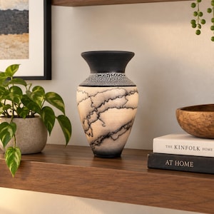 May include: A ceramic vase with a flared rim, featuring a matte black neck and base. The body displays a cream-colored surface with intricate, dark, lightning-like crackle patterns and a textured, speckled band just below the neck opening.